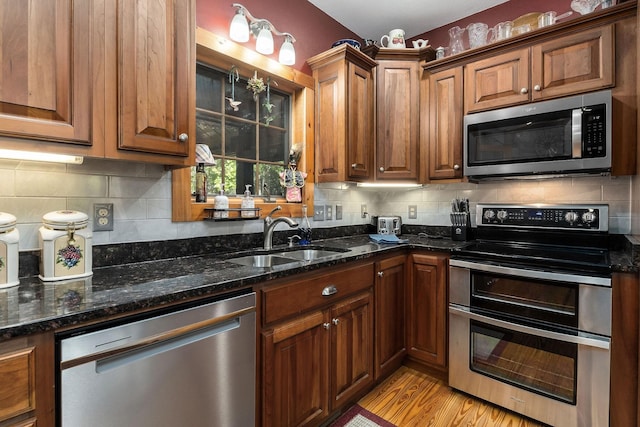 kitchen with tasteful backsplash, light wood-type flooring, a sink, dark stone counters, and stainless steel appliances