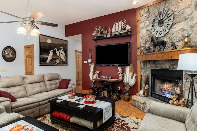 living room featuring a stone fireplace, a ceiling fan, and wood finished floors