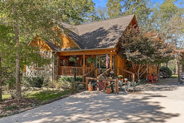 view of side of property featuring roof with shingles, covered porch, and stone siding