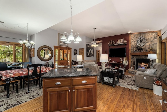 kitchen featuring a stone fireplace, light wood-style flooring, open floor plan, vaulted ceiling, and pendant lighting