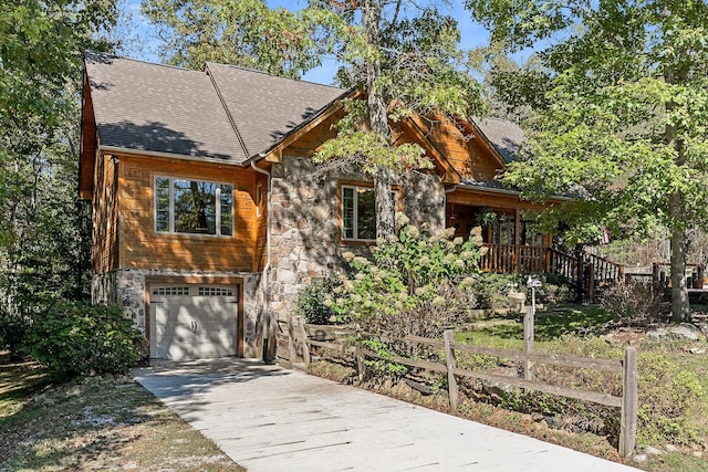 chalet / cabin with driveway, fence, an attached garage, a shingled roof, and stone siding