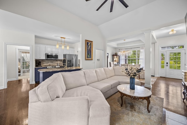living area featuring baseboards, ceiling fan with notable chandelier, and dark wood-type flooring