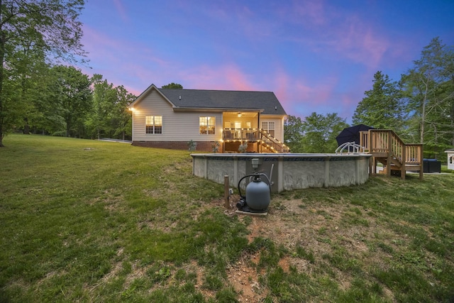 back of house at dusk with a yard, a wooden deck, stairs, and an outdoor pool