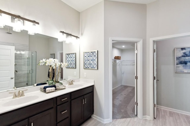 full bath with double vanity, a sink, a walk in closet, and a stall shower
