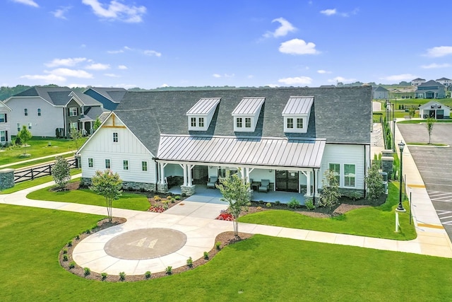 view of front of house featuring a front yard, a patio, a shingled roof, board and batten siding, and a residential view