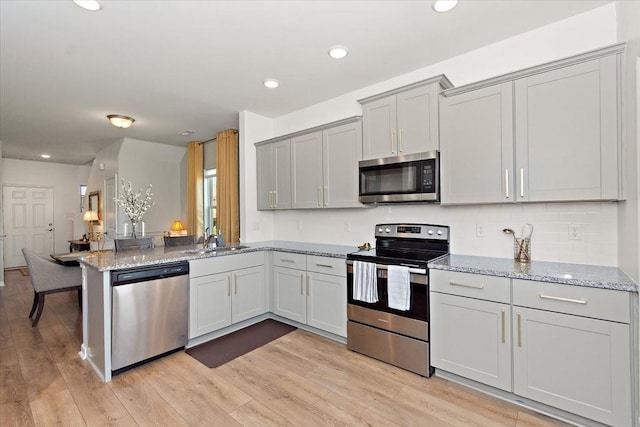 3294 Holiday Ln, Columbia, TN 38401 - kitchen featuring appliances with stainless steel finishes, a sink, light stone counters, a peninsula, and light wood-style flooring