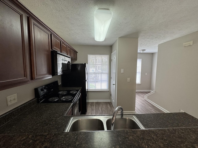 kitchen featuring a textured ceiling, dark countertops, dark brown cabinets, a sink, and black appliances