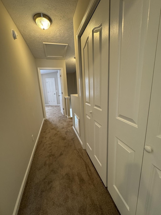 hallway with carpet floors, baseboards, attic access, and a textured ceiling