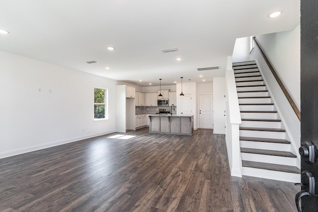 unfurnished living room featuring dark wood-style flooring, a sink, stairs, recessed lighting, and visible vents