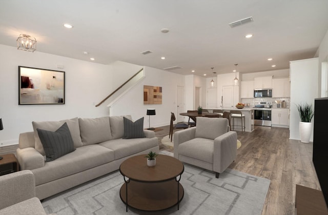 living area featuring recessed lighting, wood finished floors, visible vents, and stairway