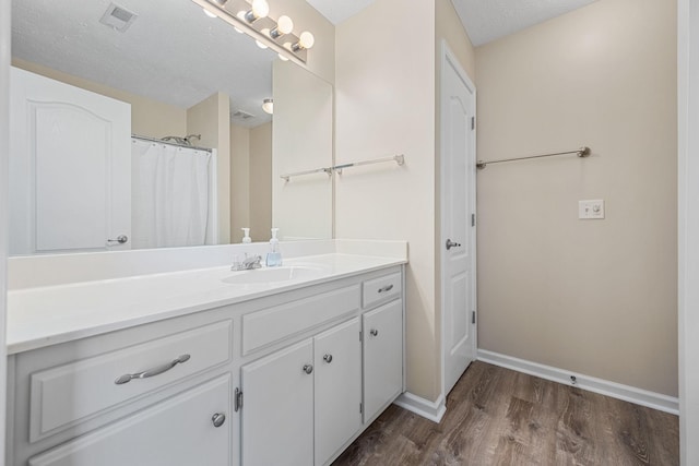 bathroom with vanity, a textured ceiling, baseboards, wood finished floors, and visible vents