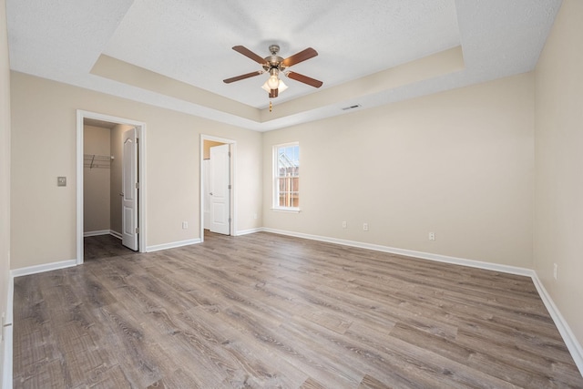 unfurnished bedroom with baseboards, a raised ceiling, wood finished floors, and a spacious closet