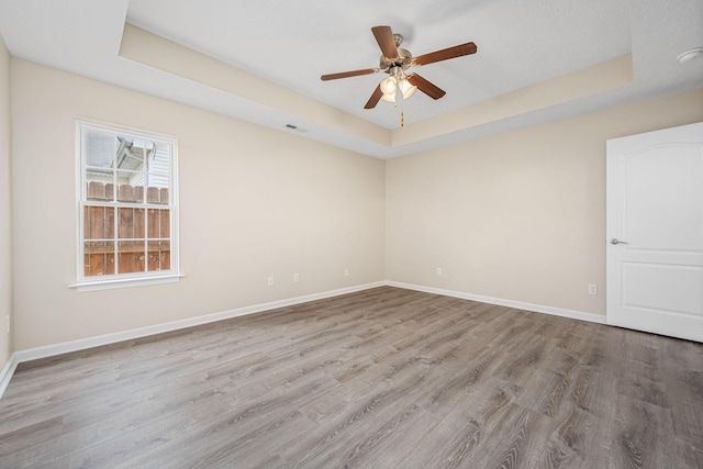 spare room featuring baseboards, ceiling fan, wood finished floors, and a raised ceiling