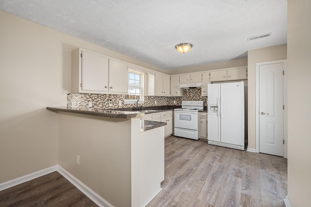 kitchen featuring visible vents, a peninsula, white appliances, under cabinet range hood, and a sink