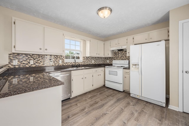 kitchen with a sink, dark countertops, under cabinet range hood, and white appliances