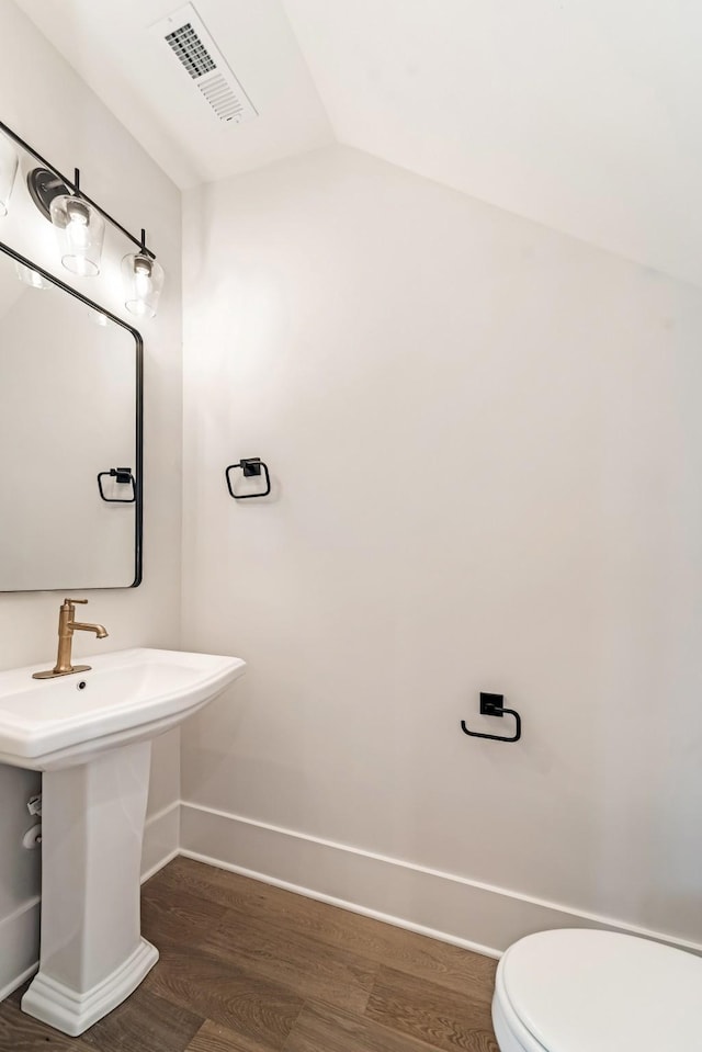 half bath with visible vents, vaulted ceiling, wood finished floors, baseboards, and toilet