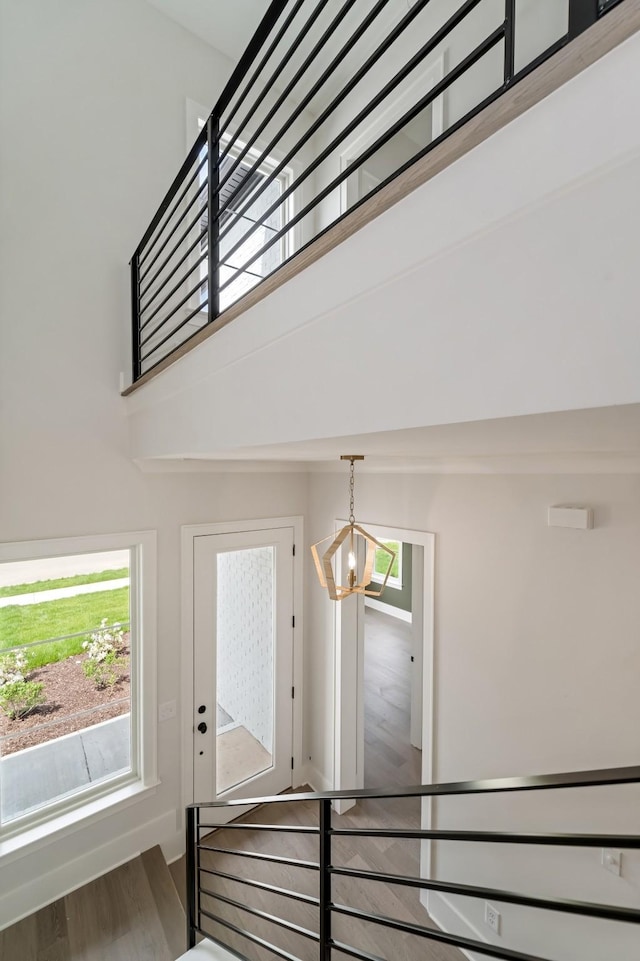 staircase with a high ceiling, a notable chandelier, a wealth of natural light, and wood finished floors