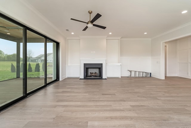 unfurnished living room featuring crown molding, a fireplace with flush hearth, a decorative wall, and light wood-type flooring