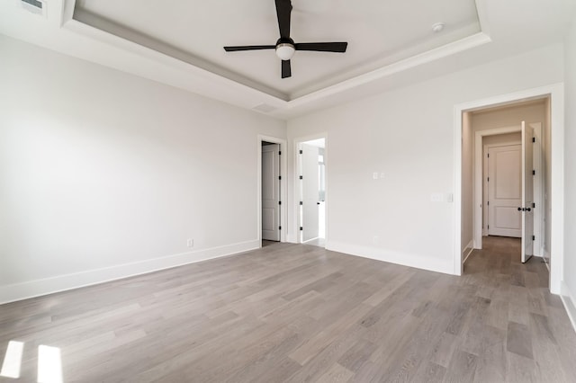 unfurnished room featuring ceiling fan, light wood finished floors, baseboards, a tray ceiling, and visible vents