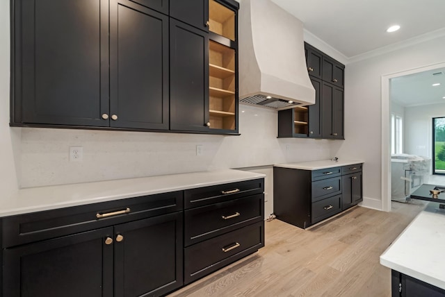 kitchen with light wood-style floors, light countertops, crown molding, and premium range hood