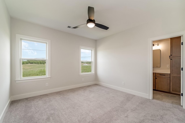 unfurnished bedroom featuring visible vents, baseboards, ceiling fan, light colored carpet, and ensuite bath