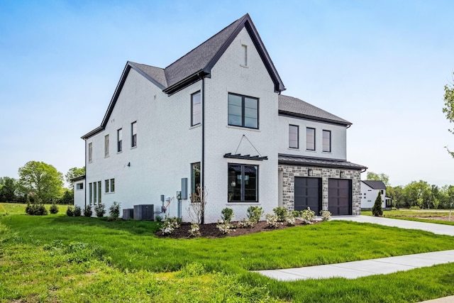 view of front of property featuring a garage, a front lawn, central AC, and driveway