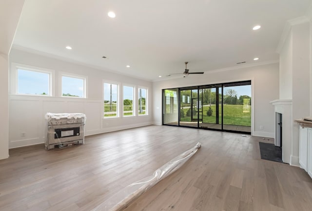 unfurnished living room with ornamental molding, a fireplace with flush hearth, ceiling fan, and a wealth of natural light