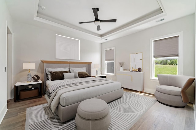 bedroom with baseboards, wood finished floors, and a tray ceiling