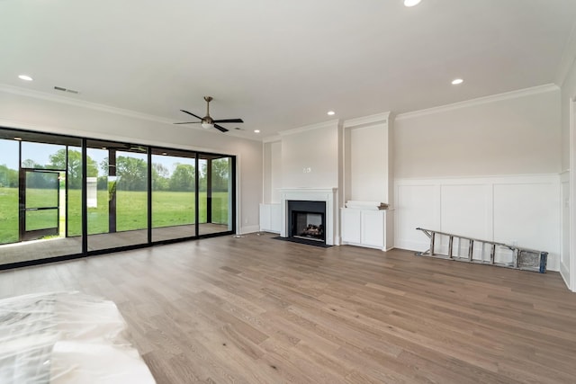 unfurnished living room with crown molding, visible vents, a decorative wall, wood finished floors, and a ceiling fan