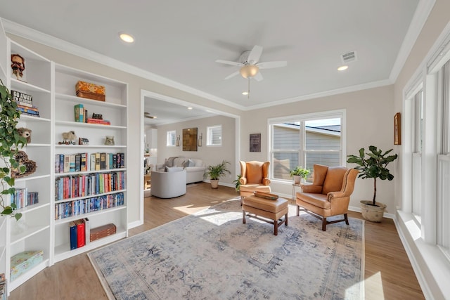 sitting room with plenty of natural light, a ceiling fan, visible vents, wood finished floors, and ornamental molding