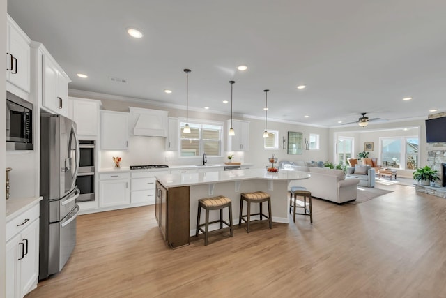 kitchen with custom range hood, a sink, open floor plan, ornamental molding, and stainless steel appliances