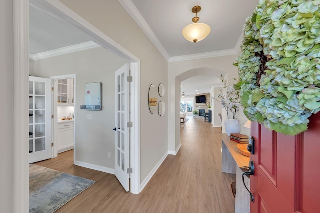 foyer featuring crown molding, arched walkways, french doors, and light wood-style flooring