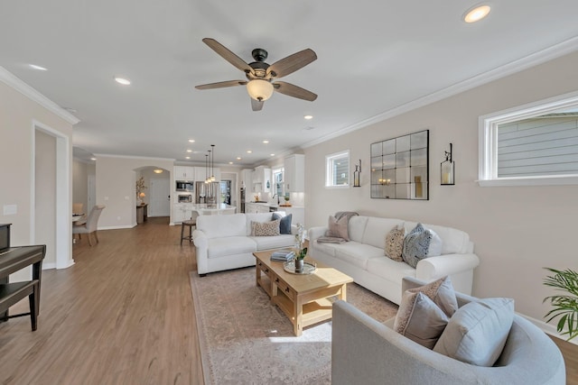 living room featuring crown molding, light wood-style floors, ceiling fan, recessed lighting, and arched walkways