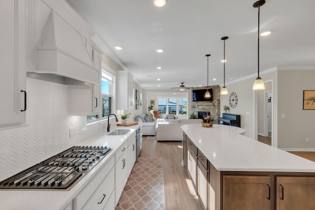 kitchen with stainless steel gas cooktop, a fireplace, ceiling fan, a sink, and light wood finished floors
