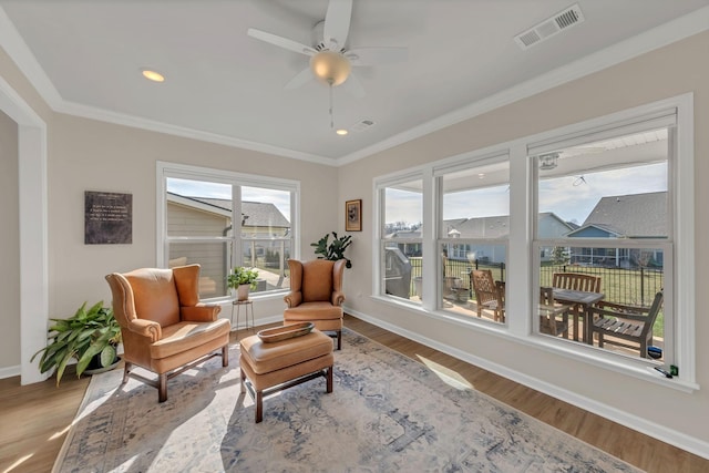 sitting room with ornamental molding, a ceiling fan, wood finished floors, and visible vents