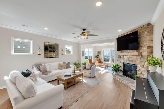 living area with crown molding, visible vents, light wood-style floors, a stone fireplace, and a ceiling fan