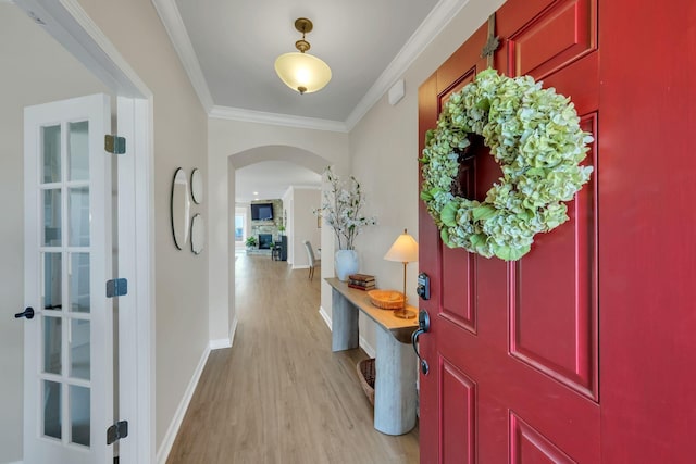entrance foyer featuring arched walkways, ornamental molding, baseboards, and light wood-style flooring