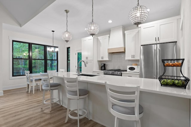 kitchen featuring freestanding refrigerator, stove, premium range hood, light countertops, and a sink
