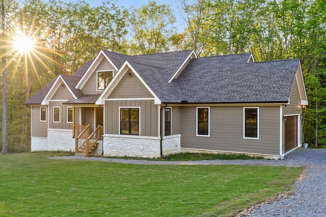 craftsman-style home with board and batten siding, driveway, a front lawn, a shingled roof, and stone siding