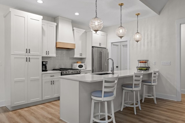 kitchen featuring a breakfast bar, light wood-style flooring, white microwave, custom exhaust hood, and high quality fridge
