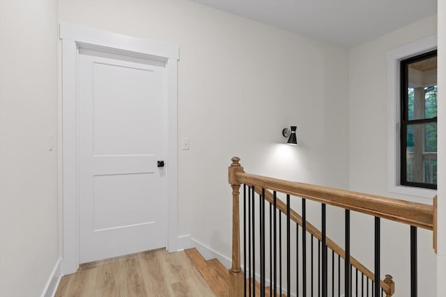 hallway with baseboards, light wood-style flooring, and an upstairs landing