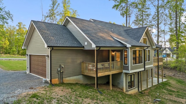back of property featuring driveway, roof with shingles, a deck, a yard, and an attached garage