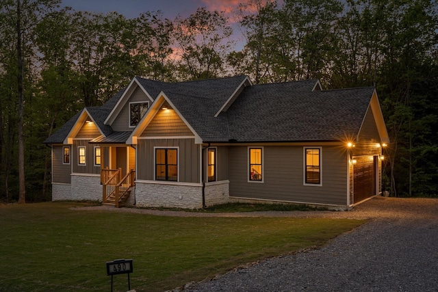 craftsman house with board and batten siding, a lawn, a garage, gravel driveway, and stone siding