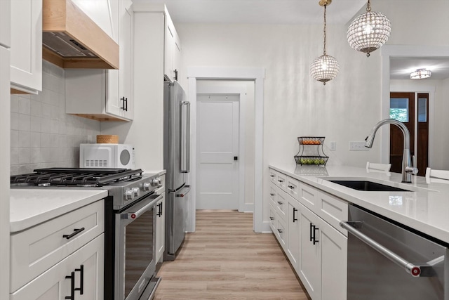 kitchen with white cabinets, appliances with stainless steel finishes, a sink, light wood-style flooring, and custom range hood