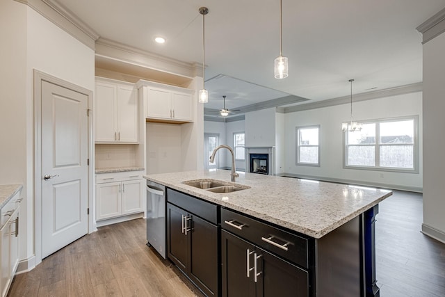 kitchen featuring stainless steel dishwasher, a fireplace, a sink, ornamental molding, and white cabinetry