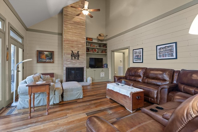 living room with high vaulted ceiling, a ceiling fan, wood walls, and hardwood / wood-style floors
