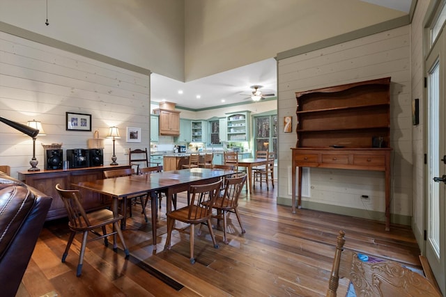dining area with wooden walls, ceiling fan, and dark wood finished floors