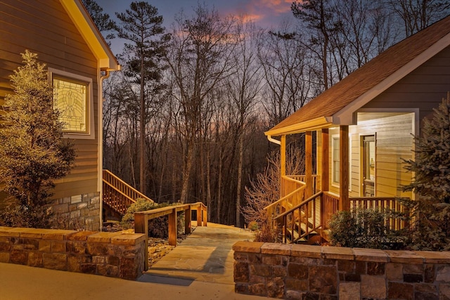 property exterior at dusk featuring stairs and roof with shingles