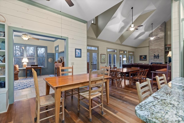 dining area with ceiling fan, french doors, wood walls, high vaulted ceiling, and wood-type flooring