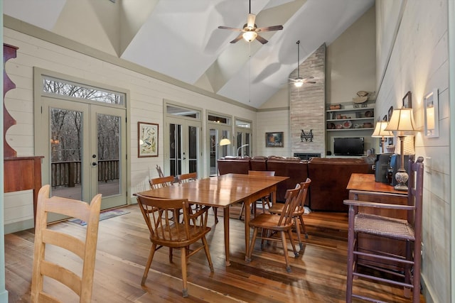 dining space featuring ceiling fan, a fireplace, high vaulted ceiling, french doors, and wood finished floors
